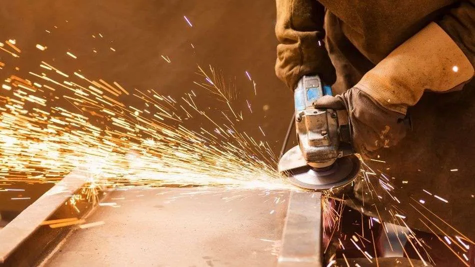 Worker grinding metal, producing bright sparks and wearing safety gloves.
